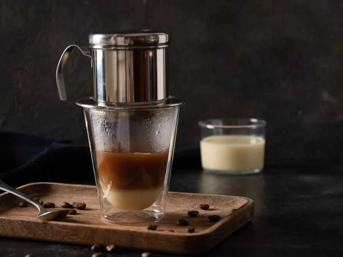 A Vietnamese phin filter dripping coffee into a glass of condensed milk